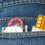 Gezeigt wird die Protasche einer dunkelblauen Jeans mit einem Tabletten Blister und einem halb ausgepackten Kondom. Das Bild möchte Stellung nehmen zum Thema Verhütung und Safer Sex .