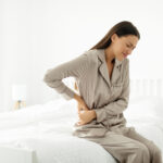 Das Foto zeigt eine junge Frau die sich die rechte Flanke beziehungsweise den Unterbauch schmerzgeplagt hält.