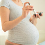 Gezeigt wird eine Schwangere Frau die sich mit einem automatisierten Gerät in eine Fingerbeere sticht um den Blutzucker zu überwachen.