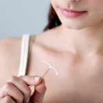 Gezeigt wird eine junge Frau die zwischen Daumen und Zeigefinger eine Kupferspirale hält .