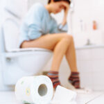 Das Bild zeigt eine kranke, ungesunde junge Frau, die an Durchfall, Blasenentzündung oder Regelschmerzen leidet, in der Toilette.