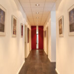 Das Bild zeigt den Flur unserer Praxis, mit Spiegelschrank am Ende des Raumes Und mehreren Bildern an der Wand.