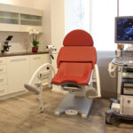 Das Bild zeigt einerseits einen gynäkologischen Behandlungsstuhl und andererseits einen Ultraschallgerät. Auf diesem Symbolisch dargestellt ein Kind im Mutterleib.