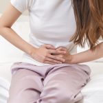 Frau mit Unterbauchschmerzen an der Bettkante sitzend